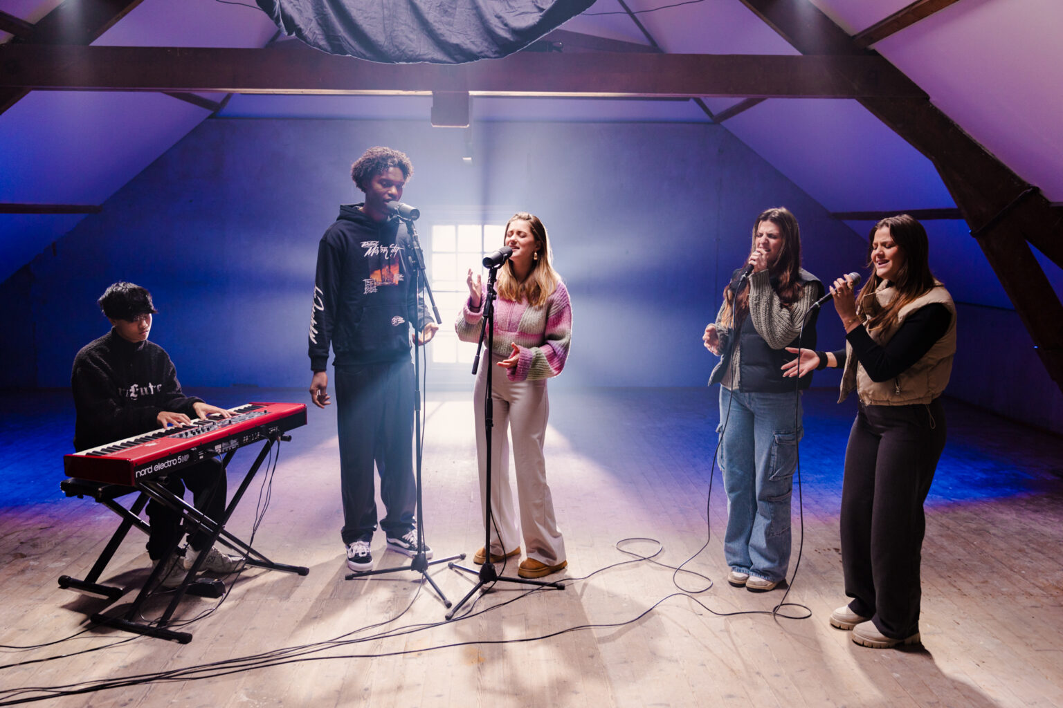 Vijf jonge muzikanten zingen en spelen keyboard op een zolder in blauw en paars licht